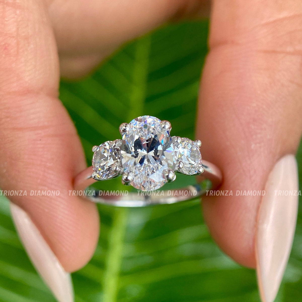 Oval cut moissanite three stone engagement ring featuring round prong set side stones