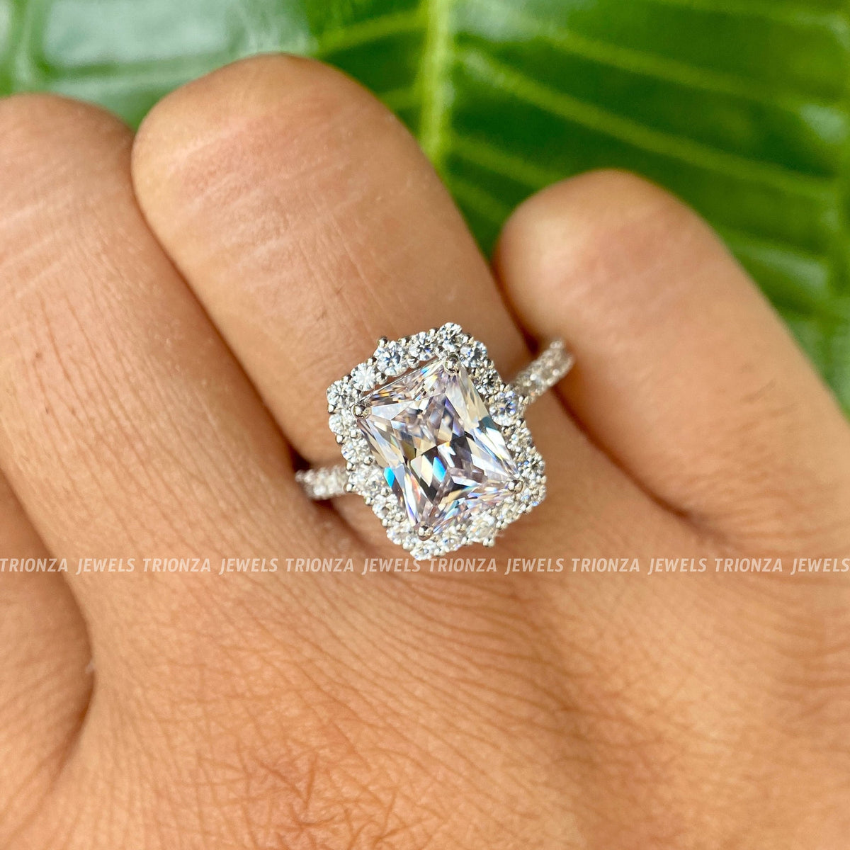 Round moissanite side stones surrounding the 3 CT radiant cut center in a prong halo design