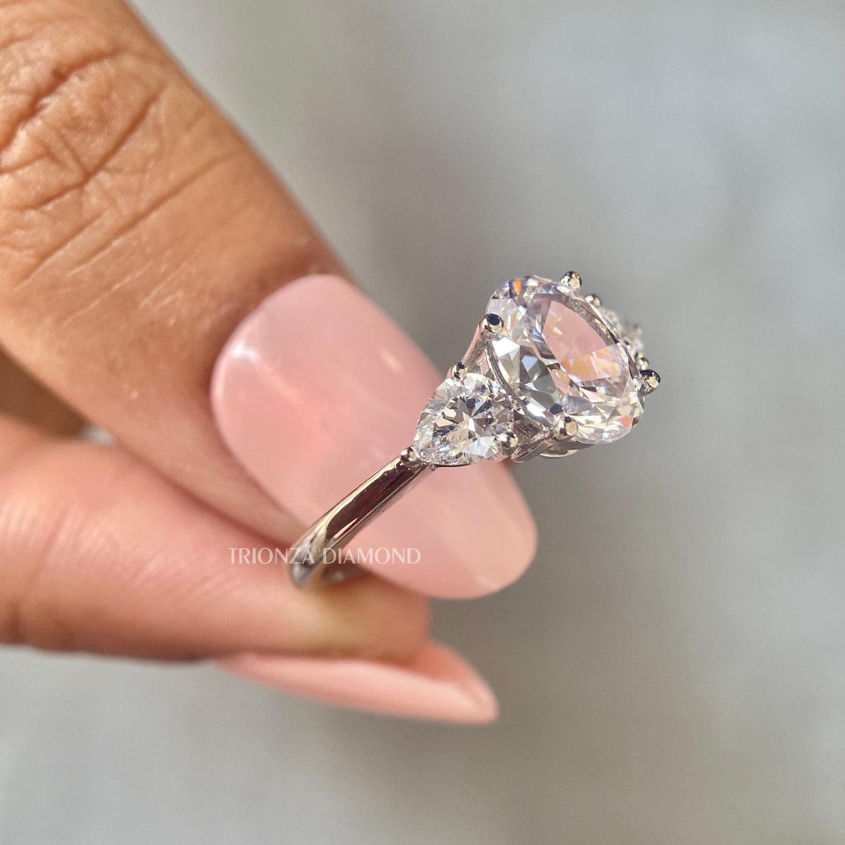 Three stone bridal ring showing the D VVS2 oval diamond paired with 0.50 carat pear side stones