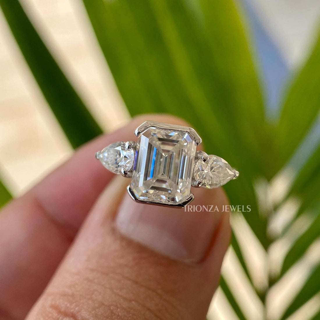 Emerald cut moissanite three stone ring featuring half bezel set side pear stones in 14k gold