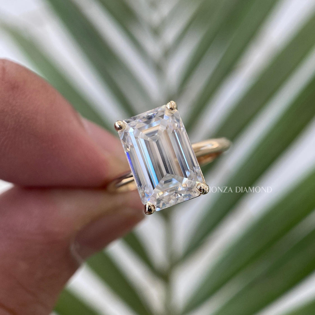 Emerald cut moissanite engagement ring displayed to show its solitaire bezel setting