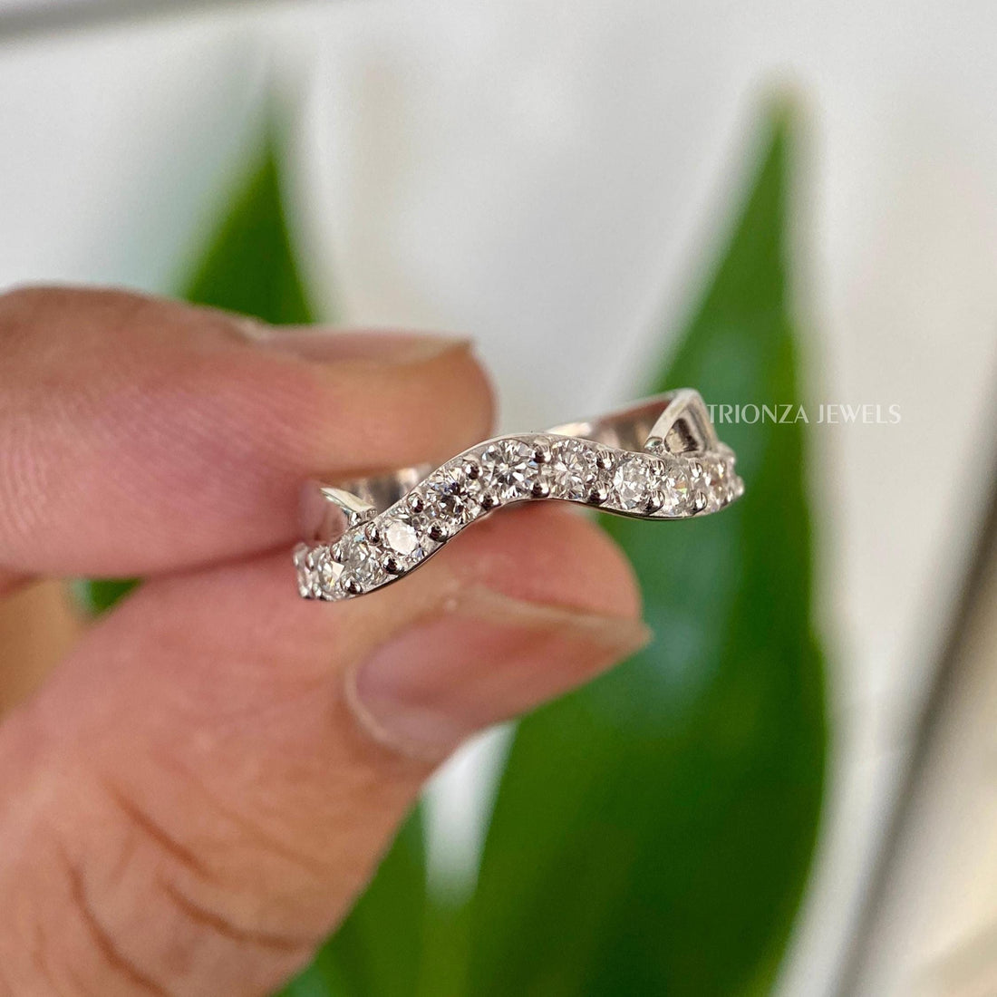 Curved half eternity wedding band featuring round cut colorless moissanite stones set in prongs
