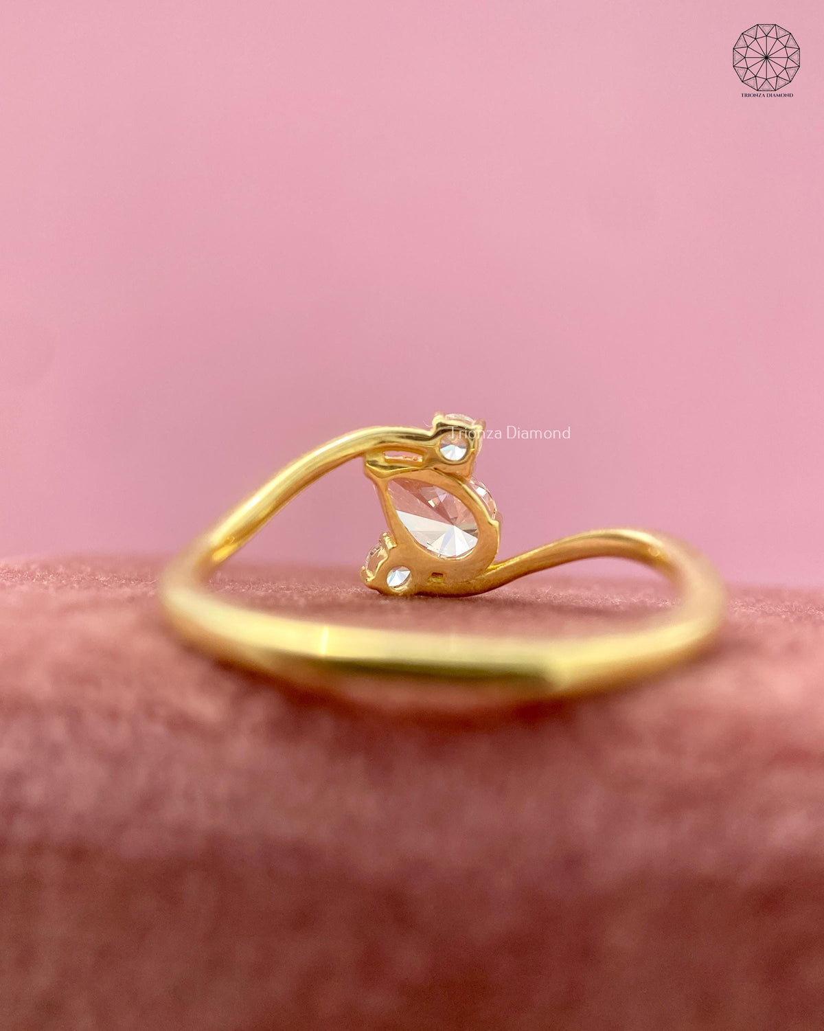 Angled view of the yellow gold swirl ring showing the pear diamond and round side stones