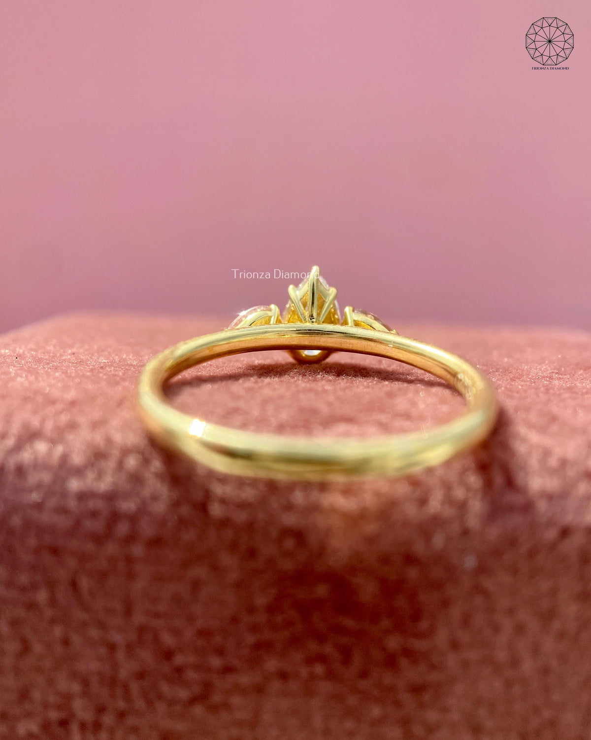 Gold trilogy ring featuring a 0.45 CT pear cut center diamond with pink side stones