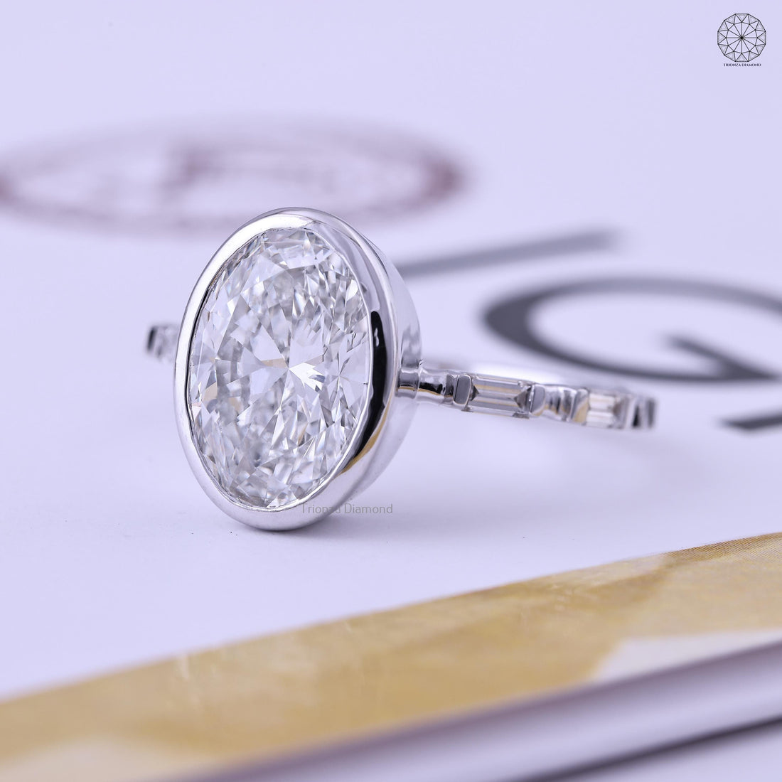 Oval lab grown diamond engagement ring with bezel setting and baguette accents in solid gold